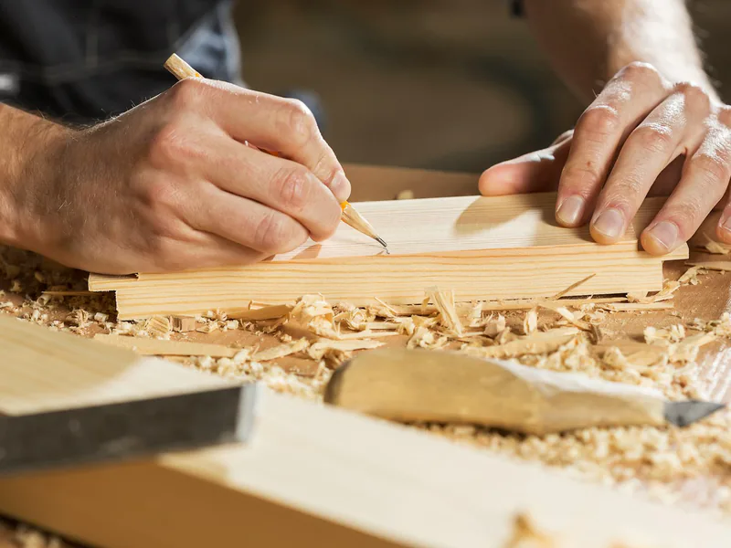 Craftsman marking a timber board with a pencil before cutting