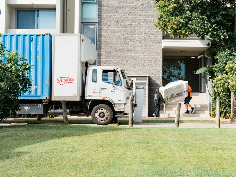 Delivery crew carrying a wrapped piece of furniture into an apartment building