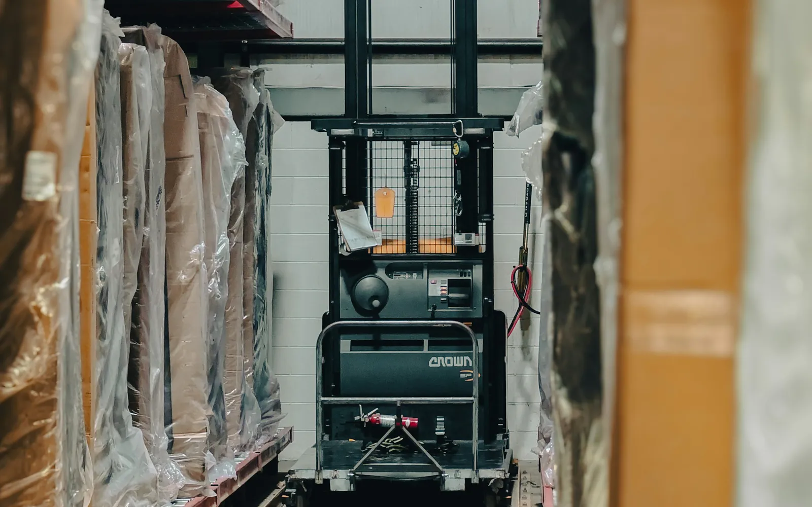 Shrink-wrapped furniture on warehouse racking beside an order picker