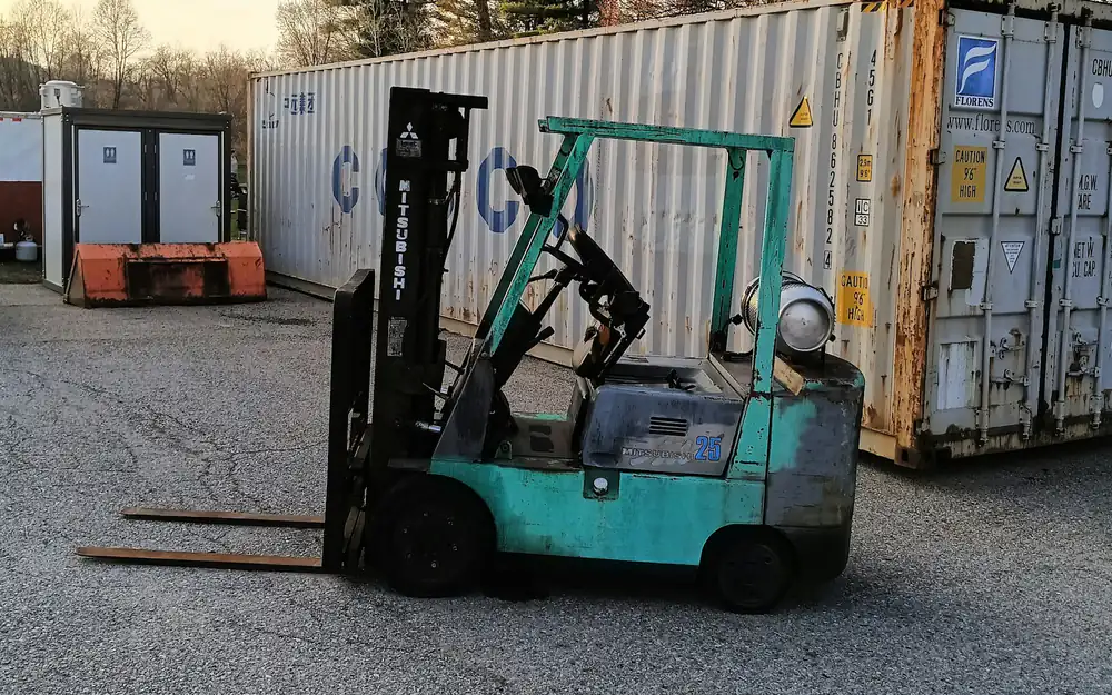 Forklift moving freight in front of stacked shipping containers