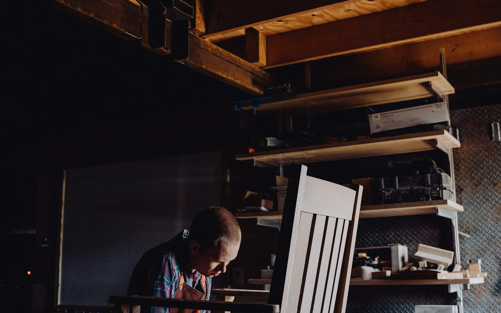 Craftsman finishing a wooden chair in a dimly lit Bali workshop